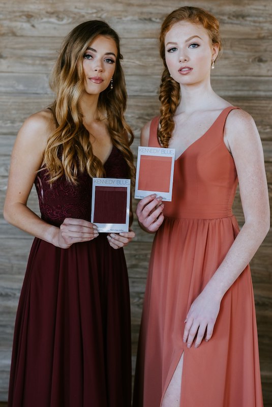 Two bridesmaids hold up color swatches that perfectly match their Kennedy Blue dresses