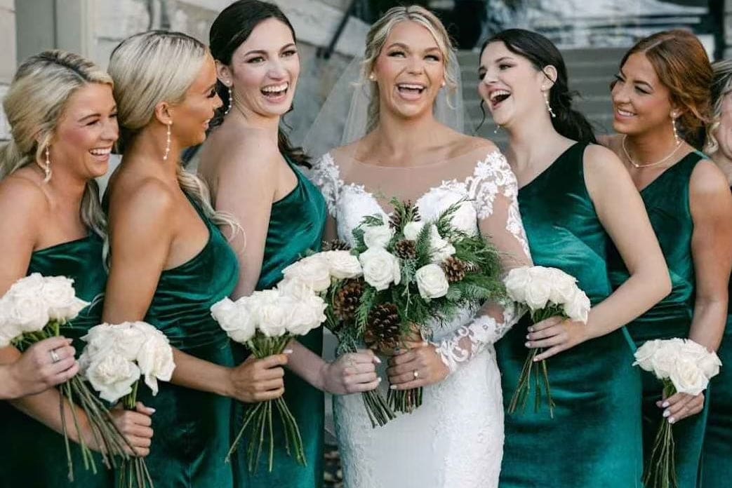 Bride with bridesmaids in teal dresses holding bouquets outdoors.