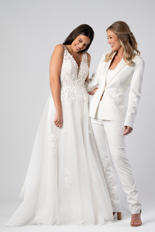 Two women wear Kennedy Blue Bridal Gown and Women's Suit